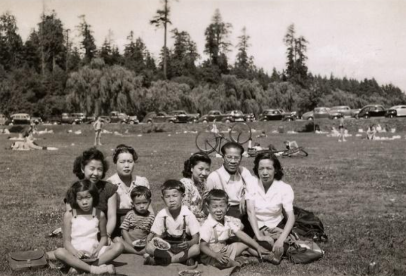 Black and white photo of family posing sitting down with children in a wide open park