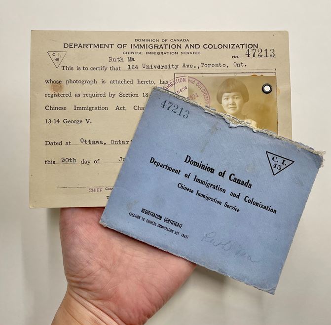 Hand holding an archival government identification from Canadian Department of Immigration and Colonization and the envelope as well as a photo on the ID of a young girl