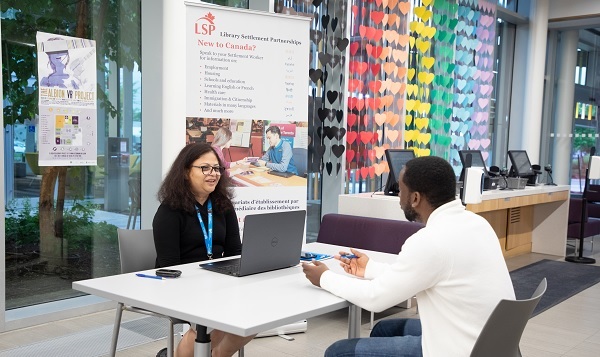 Settlement worker seated at a table and listening to the man sitting across from her Settlement worker seated at a table and listening to the man sitting across from her