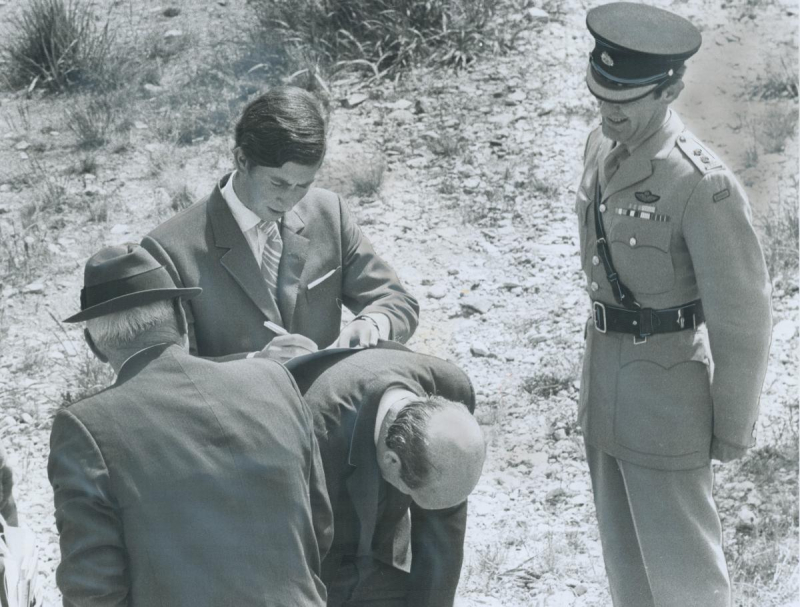 Prince Charles writes on paper on a man's back in a field