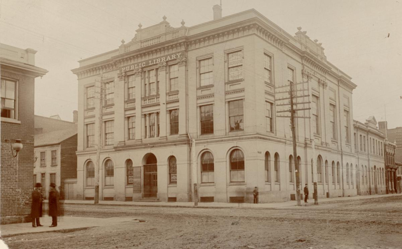 Vintage sepia photo of large corner building with sign reading Public Library