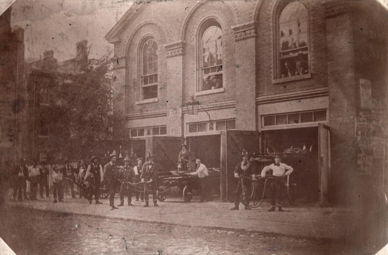 Worn vintage photo of two storey fire hall with large windows on the second storey