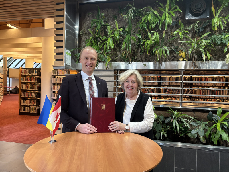 Two people standing together and holding a burgundy book inside a library Two people standing together and holding a burgundy book inside a library