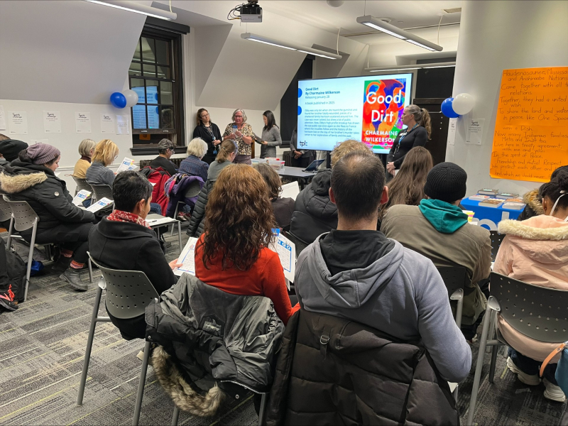 Large group of people sitting in a room watching a presentation on a screen that's led by three people Large group of people sitting in a room watching a presentation on a screen that's led by three people