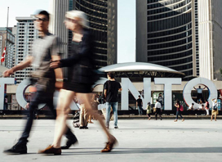 People walking in front of the Toronto sign at City Hall