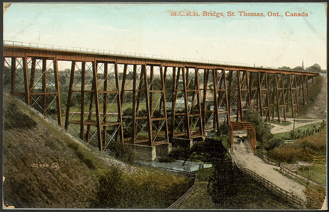 A coloured postcard of a steel trestle bridge with a roadway and trees under it.