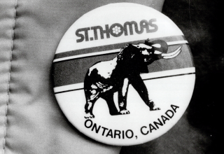 Black and white photo of a round pin with an image of an elephant on it and the words St. Thomas Ontario, Canada