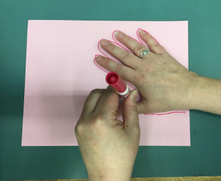 One hand tracing the outline of another on to a piece of paper.