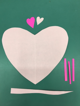 Three pink paper hearts (two small and one large), three small dark pink strips of paper, and one long light pink strip of paper.
