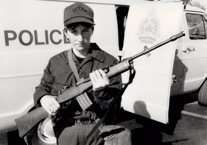 Mary Sullivan holding a rifle in front of a Hamiliton-Wentworth Regional Police truck