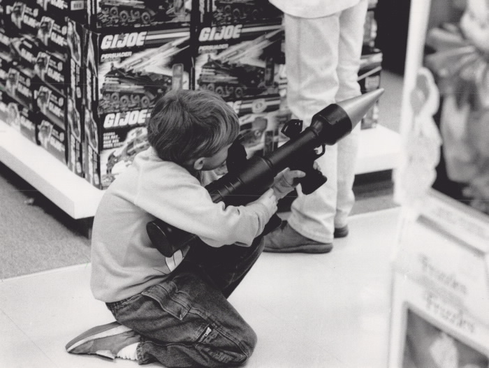 Boy crunches down and looks through the sights ofa toy rocket launcher