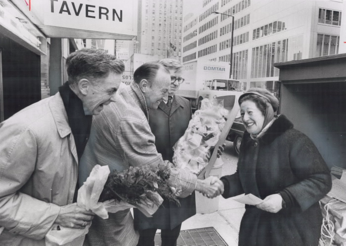 Three men happily greeting Anne Grossman at her newspaper stand