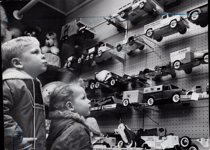 Boy and a girl stare longingly at toy trucks on the wall of a store
