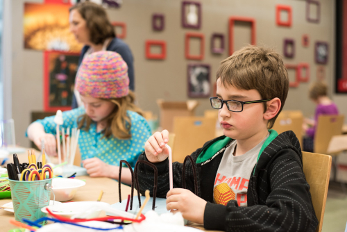 Two children sitting at a table building an object with pipecleaners