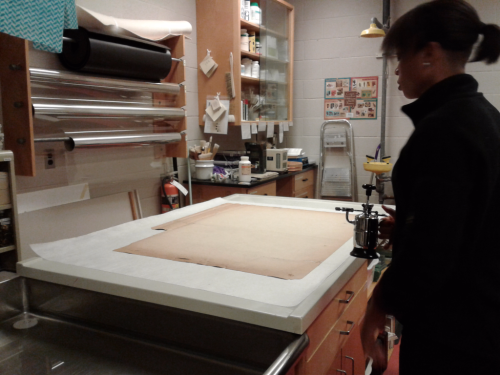 Large table in conservator lab with woman holding a tool with a nozzel