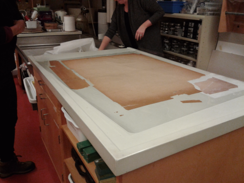 Larger poster with multiple detached pieces on table in conservation lab