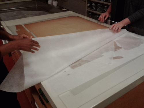 Transparen't paper being pulled by two sheets of hands to reveal a brown poster