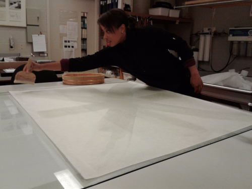 Large white paper and a woman applying substance with a tool in a conservation lab 