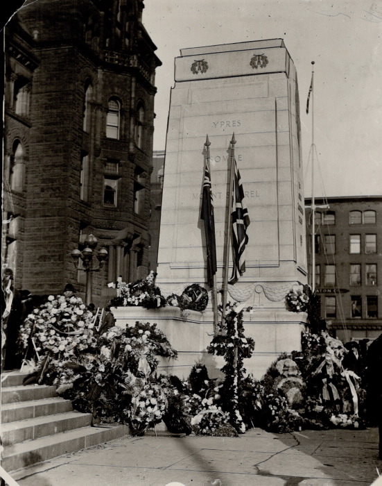 Large stone monument with flags and many flowers at base