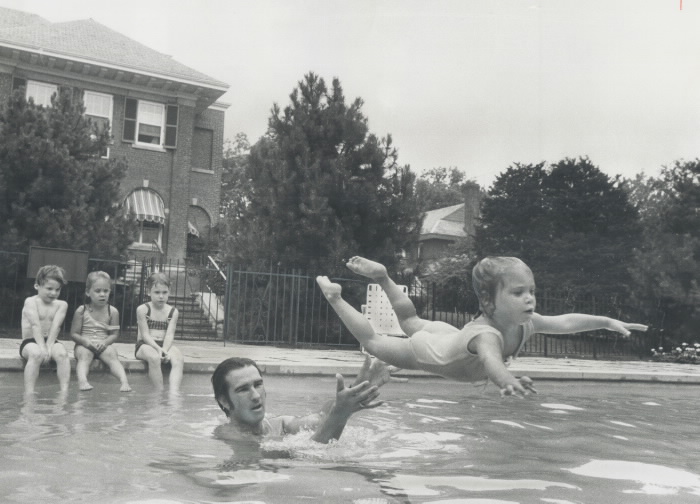 A swimming instructor standing in a pool throws a young child into the water.