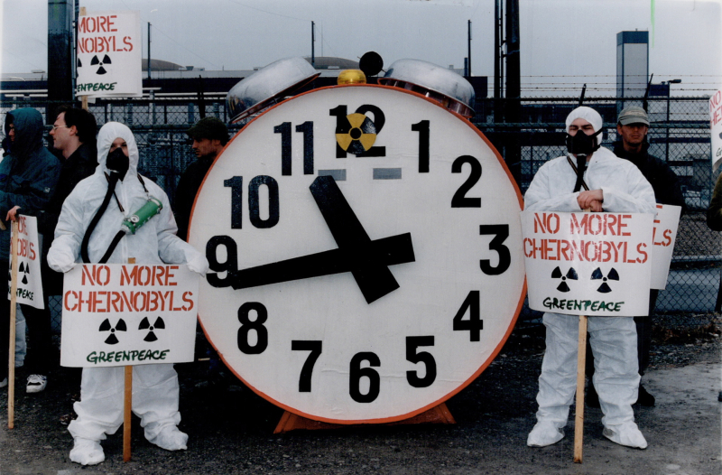 Greenpeace demonstrators donned in nuclear suits stand next to a nuclear doomsday clock
