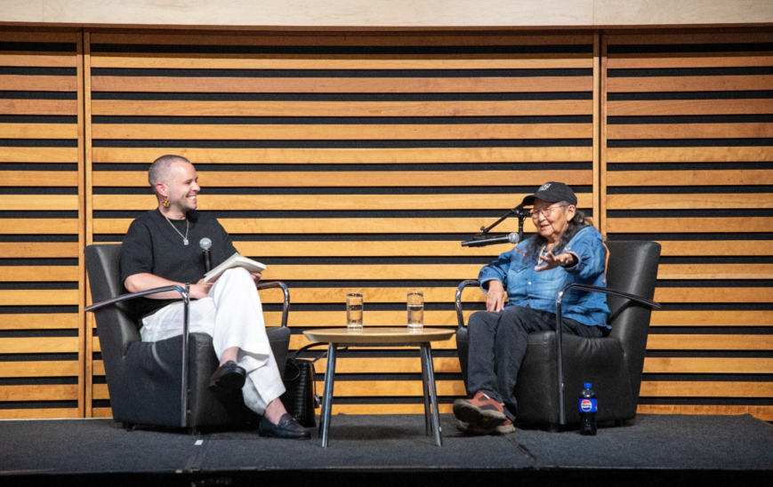A panelist and moderator interacting on a stage.