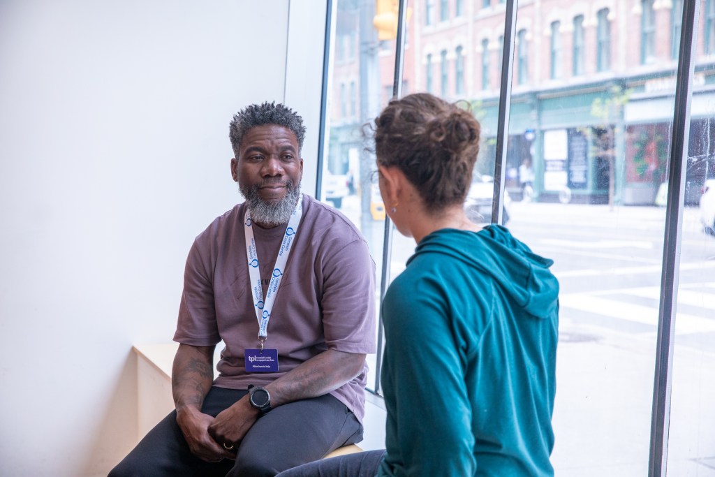 A crisis worker seated by a window with a customer.