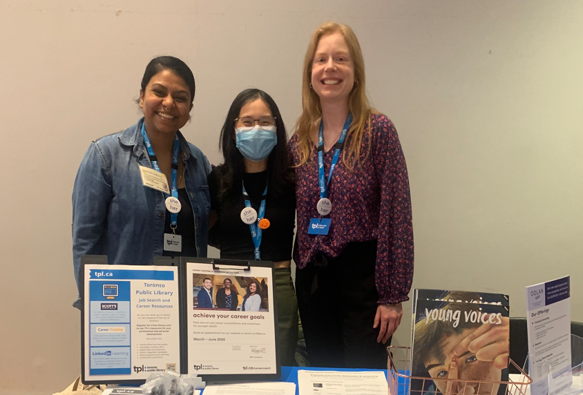 Three people standing together behind a table with flyers, smiling.